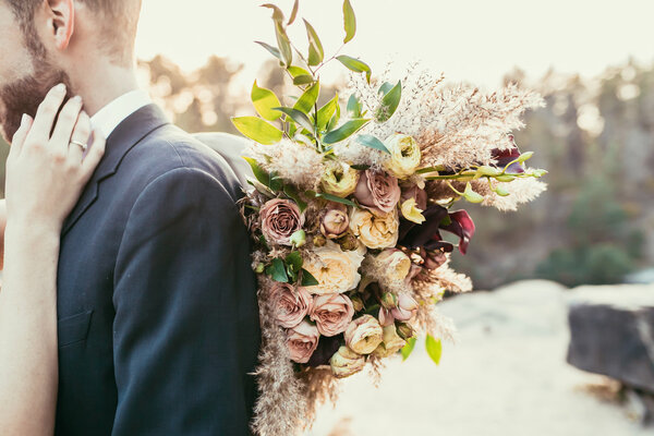 Wedding. Newlyweds. Bridal bouquet. The groom in a suit and the bride hands with a bouquet of pink flowers and greenery