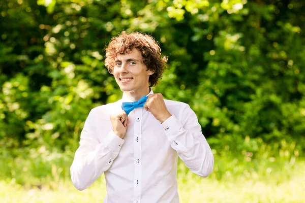 Hombre rizado en camisa blanca y pajarita azul sonriendo — Foto de Stock