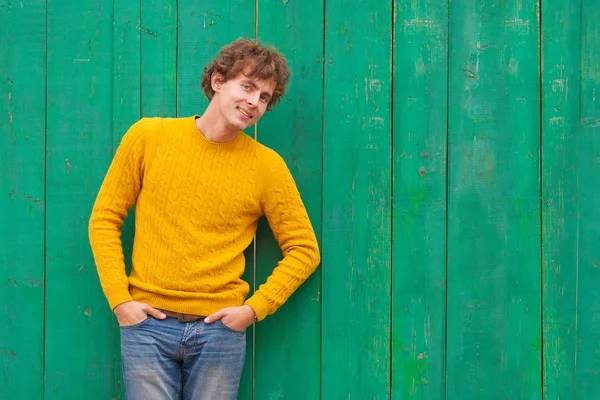 Uomo riccio sorridente in maglione giallo su sfondo verde in legno — Foto Stock