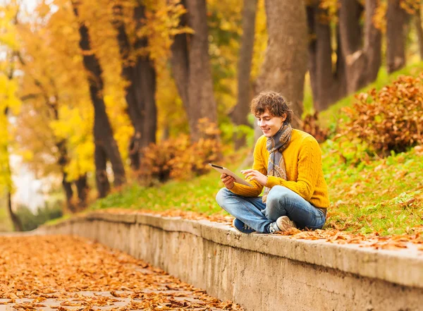 Uomo riccio con tablet computer nel parco autunnale — Foto Stock