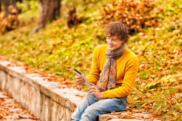 Curly man in yellow with computer tablet in autumn — Stock Photo, Image