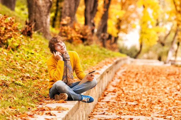 Jeune homme avec tablette et parler au téléphone en plein air — Photo