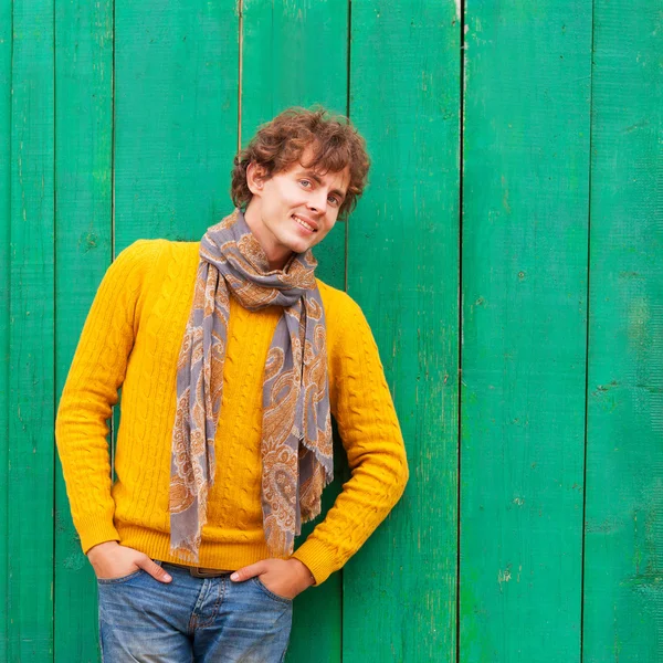 Smiling curly man in yellow sweater and scarf on green wooden ba — Stock Photo, Image