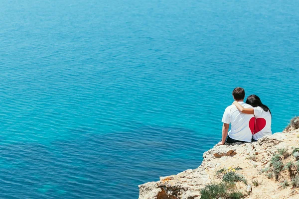 Erkek ve kadın siting cliff aşık birlikte üzerinde kalp şeklinde onların t-şort — Stok fotoğraf