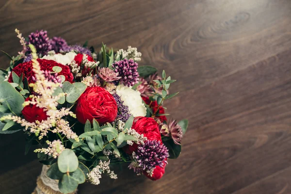 Rustikaler Hochzeitsstrauß mit roten Rosen und lila Blüten auf Holz — Stockfoto