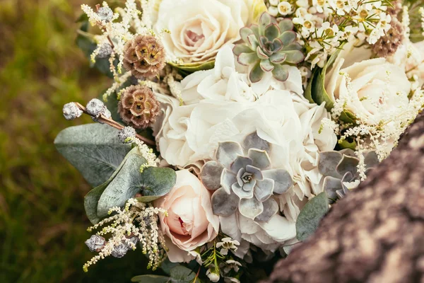 Rosen, Sukkulenten und andere Blumen im Hochzeitsstrauß auf grünem Gras und hölzerner Textur — Stockfoto