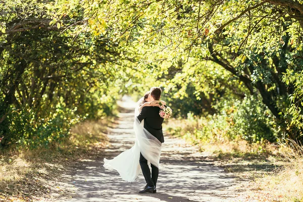 Glada brudgummen och bruden gå runt på bröllopsdag i parken vid summan — Stockfoto