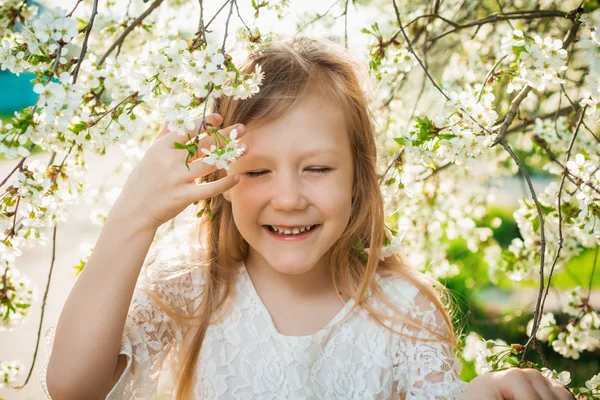 Menina em um vestido branco em um jardim de primavera ensolarado — Fotografia de Stock