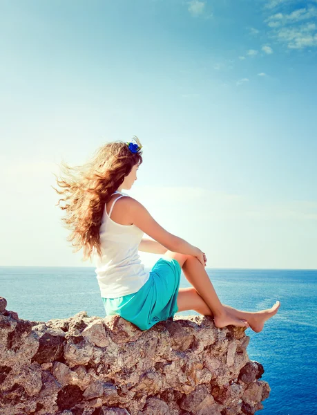 Young beautiful girl sits on a hill and looking at the sea — Stock Photo, Image