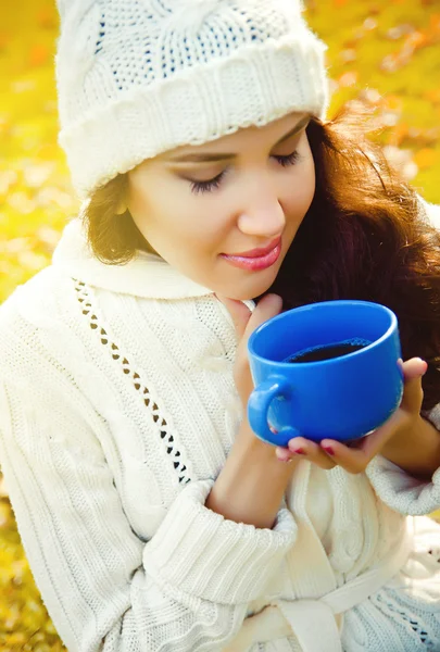 Young beautiful girl drinking a hot drink in the park — Stock Photo, Image