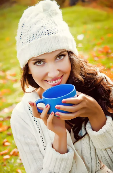 Young beautiful girl drinking a hot drink in the park — Stock Photo, Image