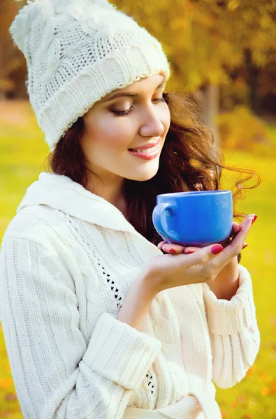 Young beautiful girl drinking a hot drink in the park — Stock Photo, Image