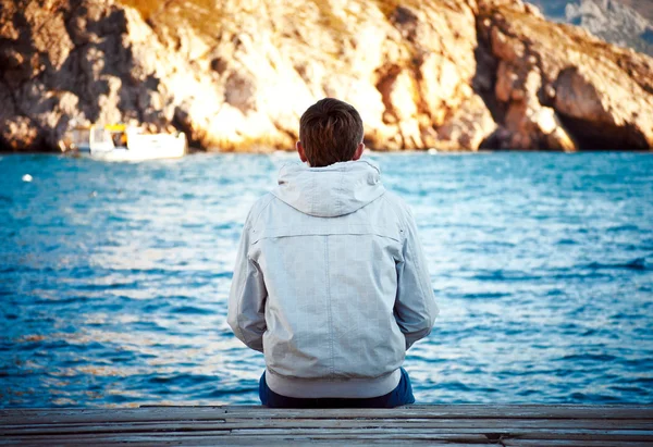 Lonely young man sitting on the dock — Stock Photo, Image