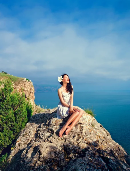 Hermosa chica se sienta en una colina sobre un fondo del mar — Foto de Stock