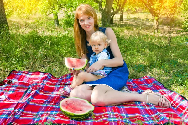 Młoda matka i dziecko siedzi w parku i jedzenie arbuza — Zdjęcie stockowe