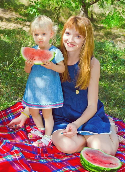 Young mother and child sitting in the park and eating watermelon — Stock Photo, Image