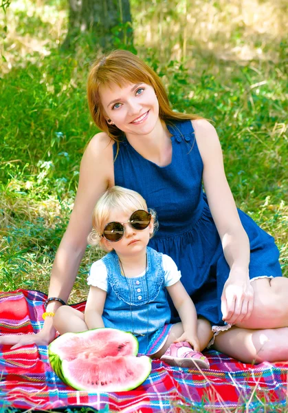 Young mother and child sitting in the park and eating watermelon — Stock Photo, Image