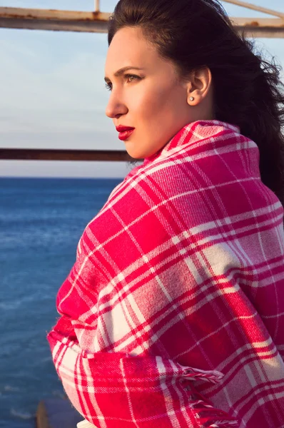 Attractive girl standing near the sea wrapped in a blanket — Stock Photo, Image