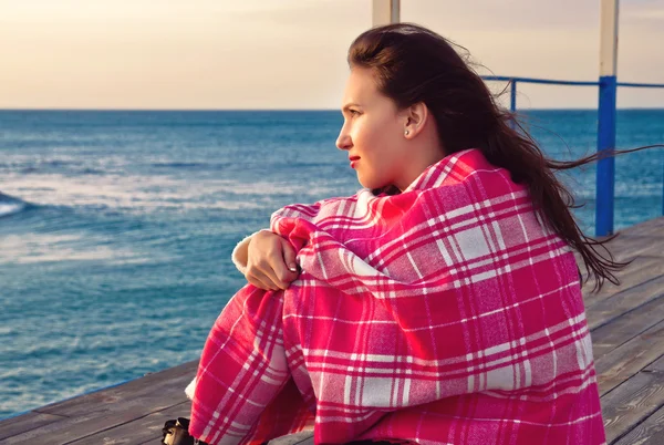 Привлекательная девушка, стоящая у моря завернутая в одеяло — стоковое фото