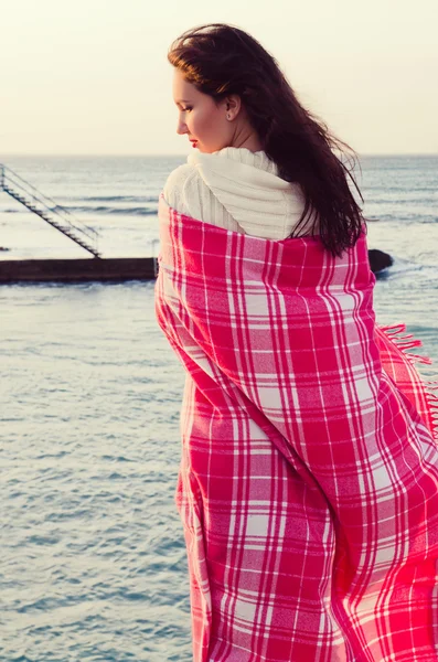 Attractive girl standing near the sea wrapped in a blanket — Stock Photo, Image