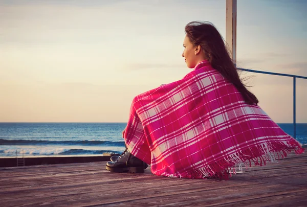 Attraktives Mädchen, das in eine Decke gehüllt am Meer steht Stockbild