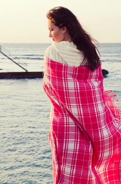 迷人的女孩站在海边裹在毯子里 免版税图库图片