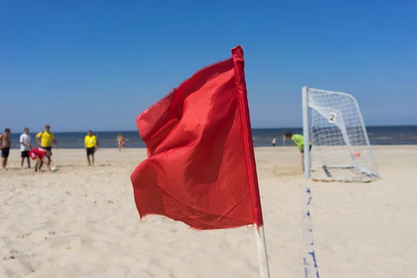 Menschen spielen Fußball am Strand vor rotem Flaggenhintergrund — Stockfoto