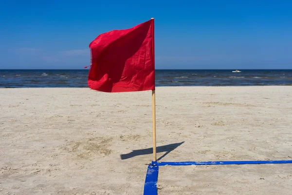 Red flag in the wind on the sandy beach — Stock Photo, Image