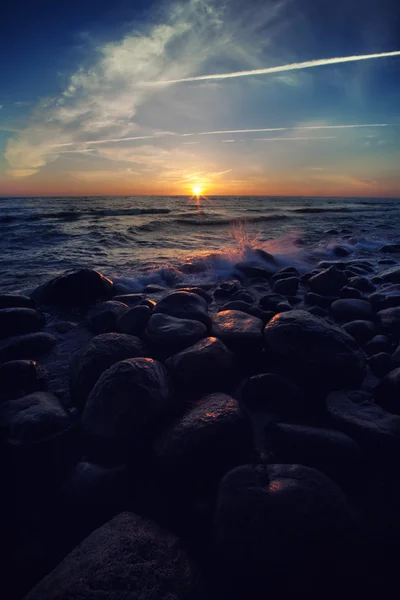 Vagues éclaboussantes sur la plage de pierres rondes au coucher du soleil — Photo