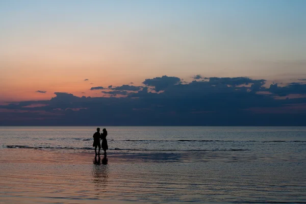 Silhouettes of young people on the beach at sunset — Stock Photo, Image