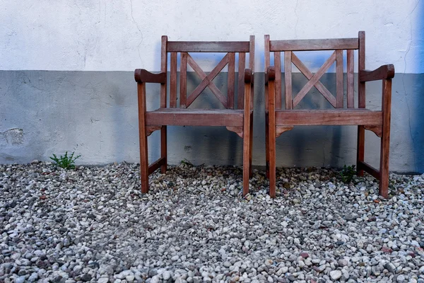 Dos sillas de madera contra una pared con piedras en el suelo —  Fotos de Stock