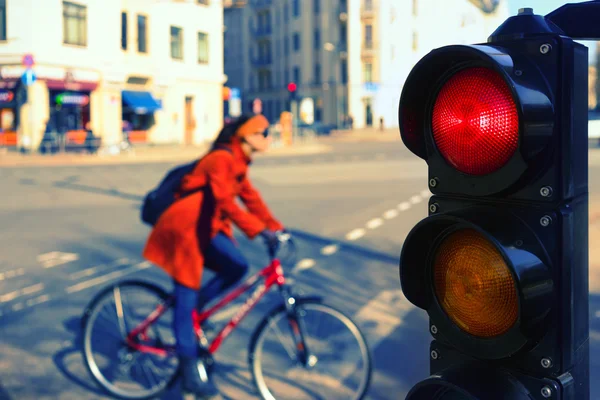 A menina em uma bicicleta em uma rua de cidade em um semáforo vermelho — Fotografia de Stock