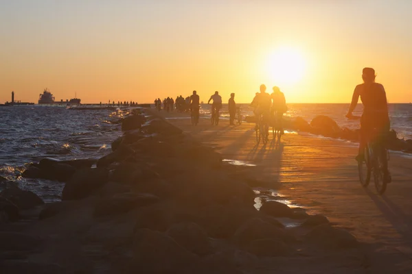 Le persone in bicicletta pedalano lungo la diga in mare al tramonto — Foto Stock