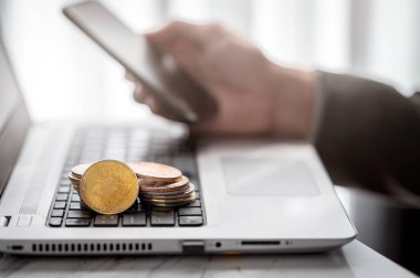 Not defterinde Bitcoin sembolü olan altın sikke yığını. Arka planda akıllı telefon kullanan işadamı eli.