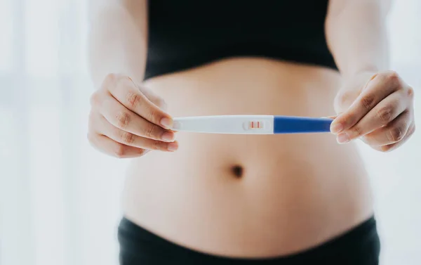 Close up shot of two month pregnant woman showing pregnancy test with positive result over her belly
