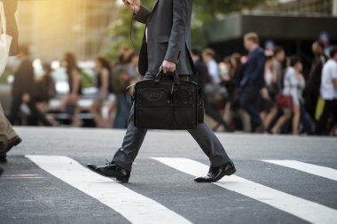 Businessman crossing the street on crosswalk and honding a laptop bag and smatphone in the city clipart