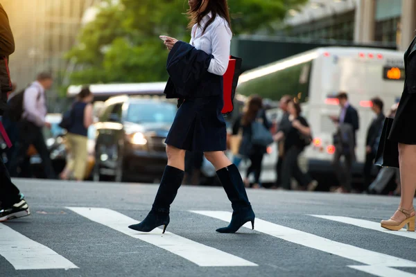 Деловая женщина ходит по пешеходной дорожке и пишет смс на смартфоне на городской улице — стоковое фото