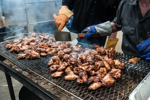Люди готовят куриные крылышки и ноги на гриле гриль уличной еды на открытом воздухе фестиваль — стоковое фото