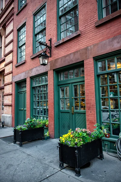 Gamla vintage rött tegel kommersiell byggnad med restaurang inne och gröna trädörrar. Blomma krukor dekoration nära byggnaden på gatan. — Stockfoto