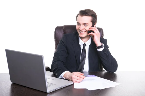 Jonge lachende zakenman werken bij het Bureau op laptop, praten op mobiele telefoon en glimlachen. — Stockfoto