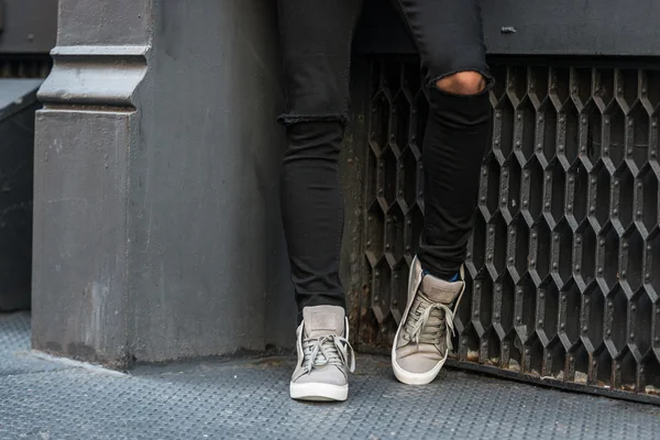 Elegante adolescente con vaqueros negros y zapatillas de deporte zapatos de pie cerca de la pared —  Fotos de Stock