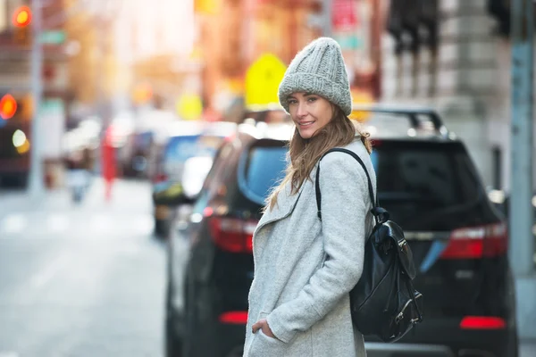 Ung vuxen kvinna gå på staden gatan bär mössa och jacka med ryggsäck. Vintern mode kvinna outfit stil — Stockfoto