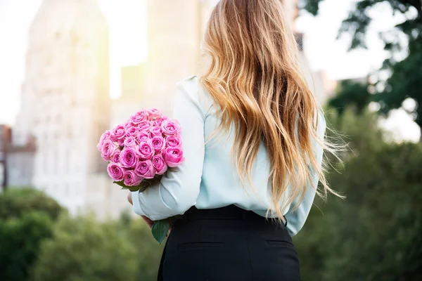 Schönes Mädchen mit einem Strauß rosa Rosen Blumen auf Dating in der Stadt. Geschäftsfrau mit Blumenstrauß. Blick von hinten. — Stockfoto