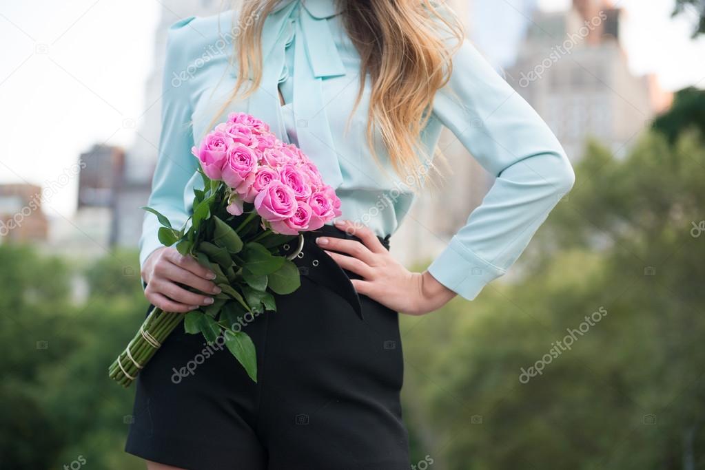 Elegant business woman holding roses bouquet against city background