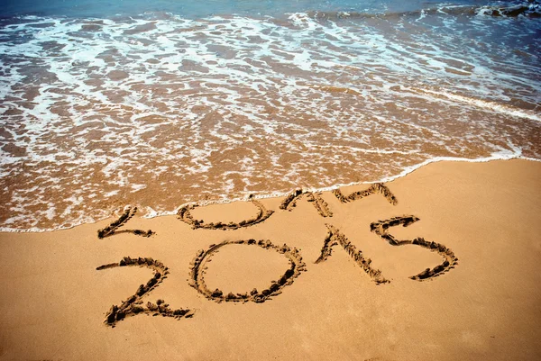 Il nuovo anno 2015 è in arrivo concetto - iscrizione 2014 e 2015 su una spiaggia di sabbia, l'onda copre cifre 2014 Immagine Stock