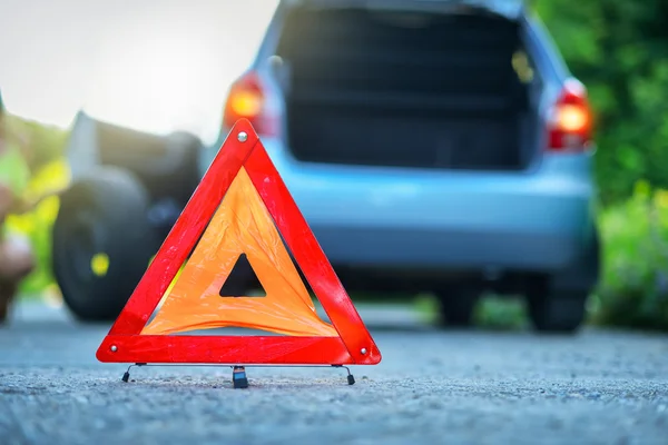 Cambiar el neumático en un coche averiado en una carretera con triángulo de advertencia rojo —  Fotos de Stock