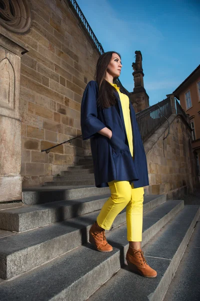 Jovem mulher bonita vestindo casaco azul, casaco amarelo posando ao ar livre . — Fotografia de Stock