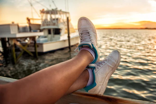 Woman legs over the sea bay and yachts at sunset time. Relaxing after runnig. — Stockfoto