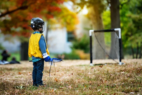 Bambino che gioca a lacrosse con il bastone nel parco autunnale . — Foto Stock