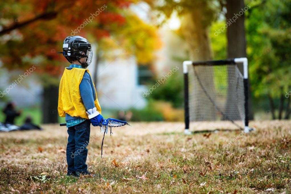 Little kid playing lacrosse with his stick in the autumn park. — Stock